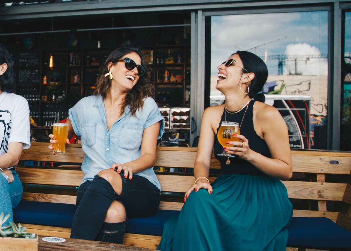 Two friends laughing together with drinks at an outdoor celebration
